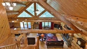 A log cabin interior with a wooden staircase, a fireplace, a dining area, and large windows. - Secluded luxury log home in Wisconsin wilderness (Clam Lake)