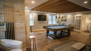 A spacious room with a pool table, wooden beams on the ceiling, and a billiards rack against the wall. - Large, Charming Cape Cod Home Close To Orleans And Chatham Beaches (Orleans)