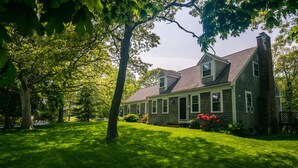 A two-story house with a gabled roof, surrounded by a well-maintained lawn and mature trees. - Large, Charming Cape Cod Home Close To Orleans And Chatham Beaches (Orleans)