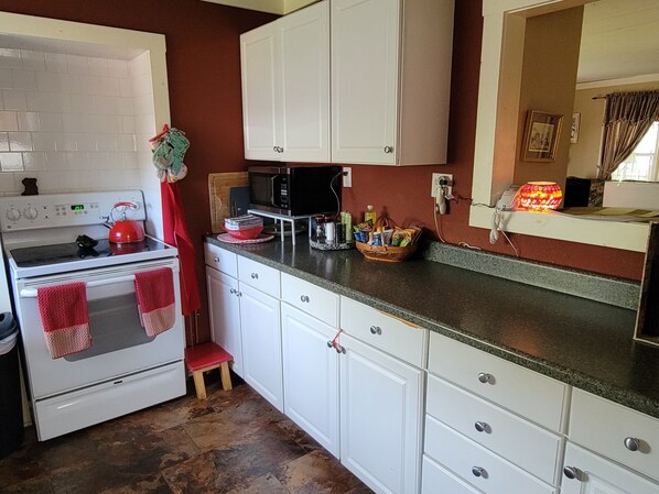 A kitchen with white cabinets, a stove, a microwave, and a small stool.