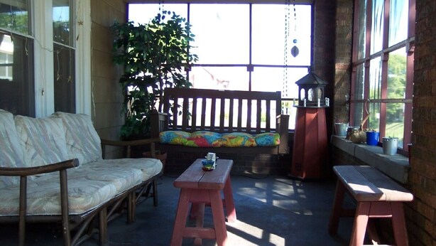A sunlit patio with a wooden bench, a cushioned sofa, and two wooden stools. - Downtown St. Joe! Walk to BEACH & EVERYTHING! Clean & Comfortable!  Best Value! (St. Joseph)