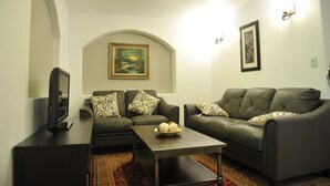 Una sala de estar con un juego de sofá, una mesa de centro, un televisor sobre un mueble bajo y un cuadro en la pared.
