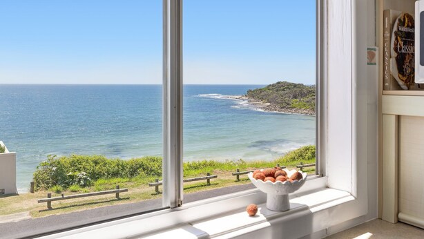 Vista costera desde una ventana con vista al mar y una isla rocosa.