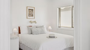 A bedroom with a bed, two bedside lamps, a framed picture, and a window.
