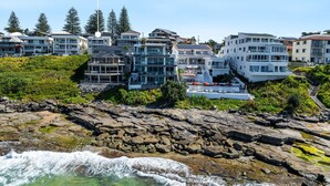 Una zona residencial costera con edificios modernos de varios pisos, costa rocosa y cielo azul despejado.
