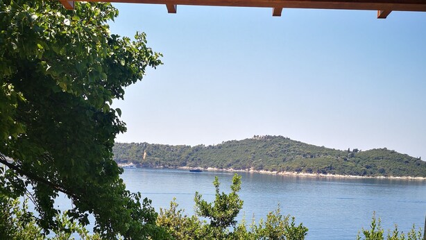 Un patio con un tavolo in mosaico, due vasi di fiori, binocoli e vista sul mare e le colline.