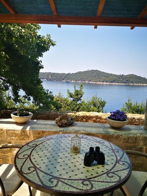 A patio with a mosaic table, two flower pots, binoculars, and a view of the sea and hills. - Blue Infinity waterfront apartment (Dubrovnik)