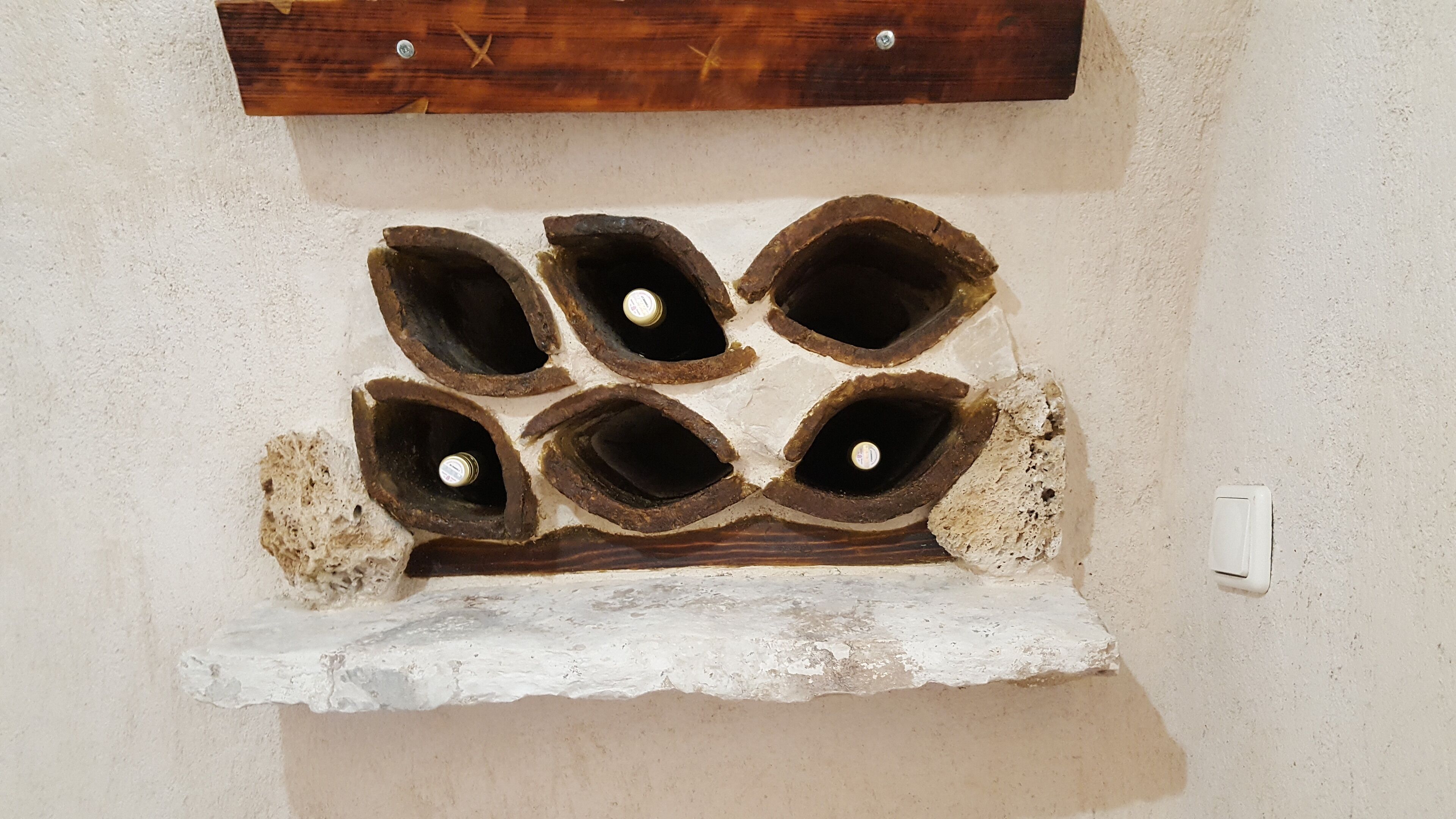 Un mur percé de six ouvertures circulaires, chacune contenant une bouteille.