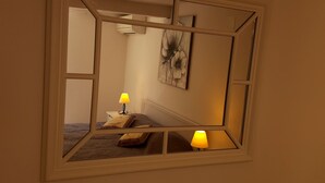 Una camera da letto con un grande specchio, un comodino con una lampada e un quadro appeso al muro.