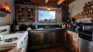 Una cocina rústica con armarios de madera, estufa, lavaplatos y ventana con vistas a árboles.