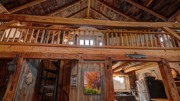 Interior rústico de madera con zona de entrepiso, vigas de madera y una escalera.