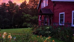 Una casa roja con techo inclinado, rodeada de un jardín con diversas plantas y flores.