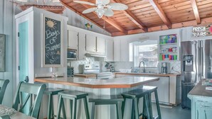 A kitchen with a central island, bar stools, a ceiling fan, and a chalkboard with writing.