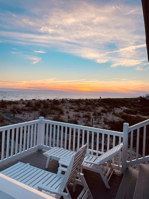 Enjoy a serene beach view from this deck, featuring two comfortable chairs and a small table.
