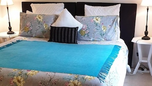 A neatly made bed with floral bedding and a blue throw, two bedside lamps, and a framed picture on the wall. -  ASTLEY  COTTAGE   SPA & KING BED WITH FREE  WIFI & Netflix (Daylesford)