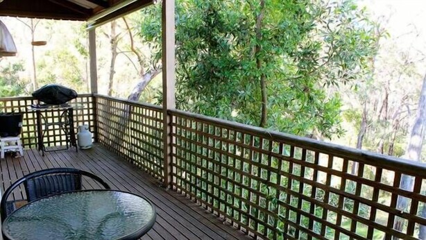 A covered outdoor deck with a glass table and chairs, surrounded by a wooden fence and lush greenery. -  ASTLEY  COTTAGE   SPA & KING BED WITH FREE  WIFI & Netflix (Daylesford)
