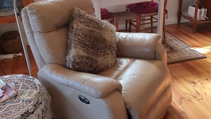A leather recliner with a fur throw, a desk with a vase of flowers, and a view of the outdoors through a window. -  ASTLEY  COTTAGE   SPA & KING BED WITH FREE  WIFI & Netflix (Daylesford)