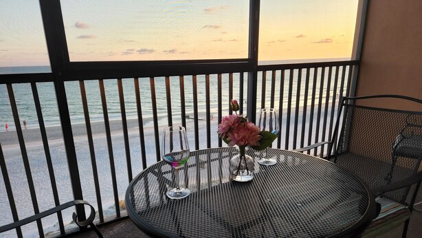 A balcony with a round metal table, two chairs, a vase with flowers, and a wine glass.