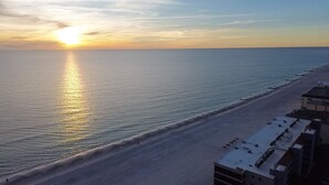 A beach with a sunset, a building with a flat roof, and a clear sky.