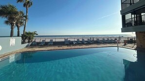 A clear blue pool with lounge chairs and a view of the beach.