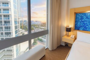 A hotel room with a large window, a bed, a bedside table with a lamp, and a painting on the wall. - Oceanfront Condominium with Breathtaking Views and Beach Access (Sunny Isles Beach)