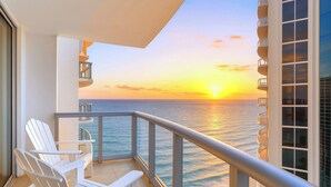 A balcony with white chairs, a railing, and a view of the ocean at sunset. - Oceanfront Condominium with Breathtaking Views and Beach Access (Sunny Isles Beach)