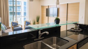 A modern kitchen with a glass island, stainless steel sink, and a flat-screen TV mounted on the wall. - Oceanfront Condominium with Breathtaking Views and Beach Access (Sunny Isles Beach)