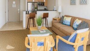 A modern living room with a sofa, two armchairs, a coffee table, and a kitchen area in the background. - Oceanfront Condominium with Breathtaking Views and Beach Access (Sunny Isles Beach)