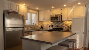 A modern kitchen with white cabinets, stainless steel appliances, a large island with bar stools, and a tiled backsplash.