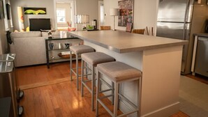 A modern kitchen with a central island, bar stools, a refrigerator, and a television.