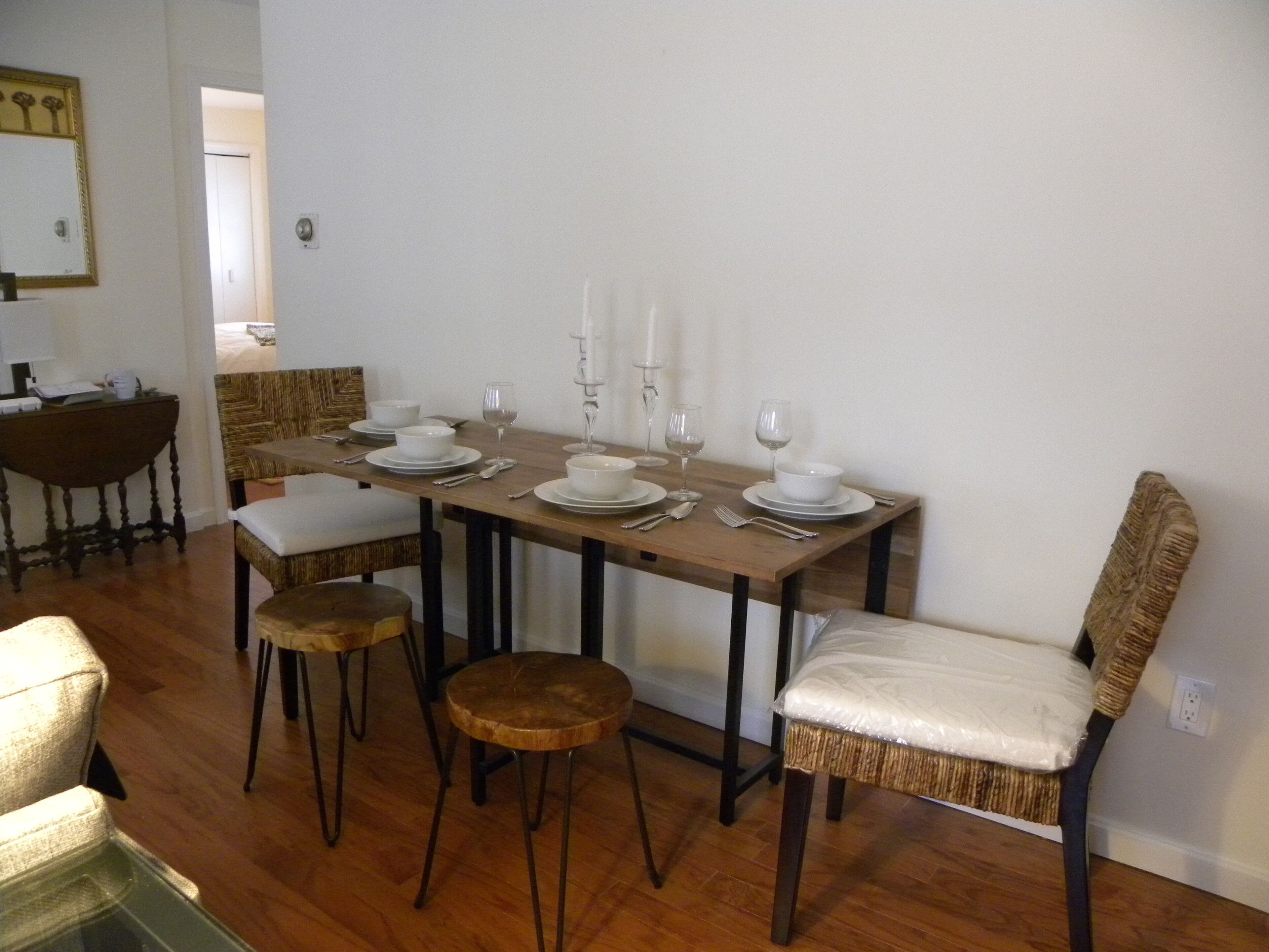 A dining area with a wooden table set for four, surrounded by four chairs with cushioned seats.
