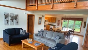 A spacious living area with a wooden floor, two sofas, a coffee table, and a dining area with a wooden table and chairs. - Large Finger Lakes Getaway - 5 BR with Bath Access! (Naples)