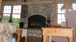 A cozy room with a stone fireplace, wooden beams, and large windows. - Large Finger Lakes Getaway - 5 BR with Bath Access! (Naples)