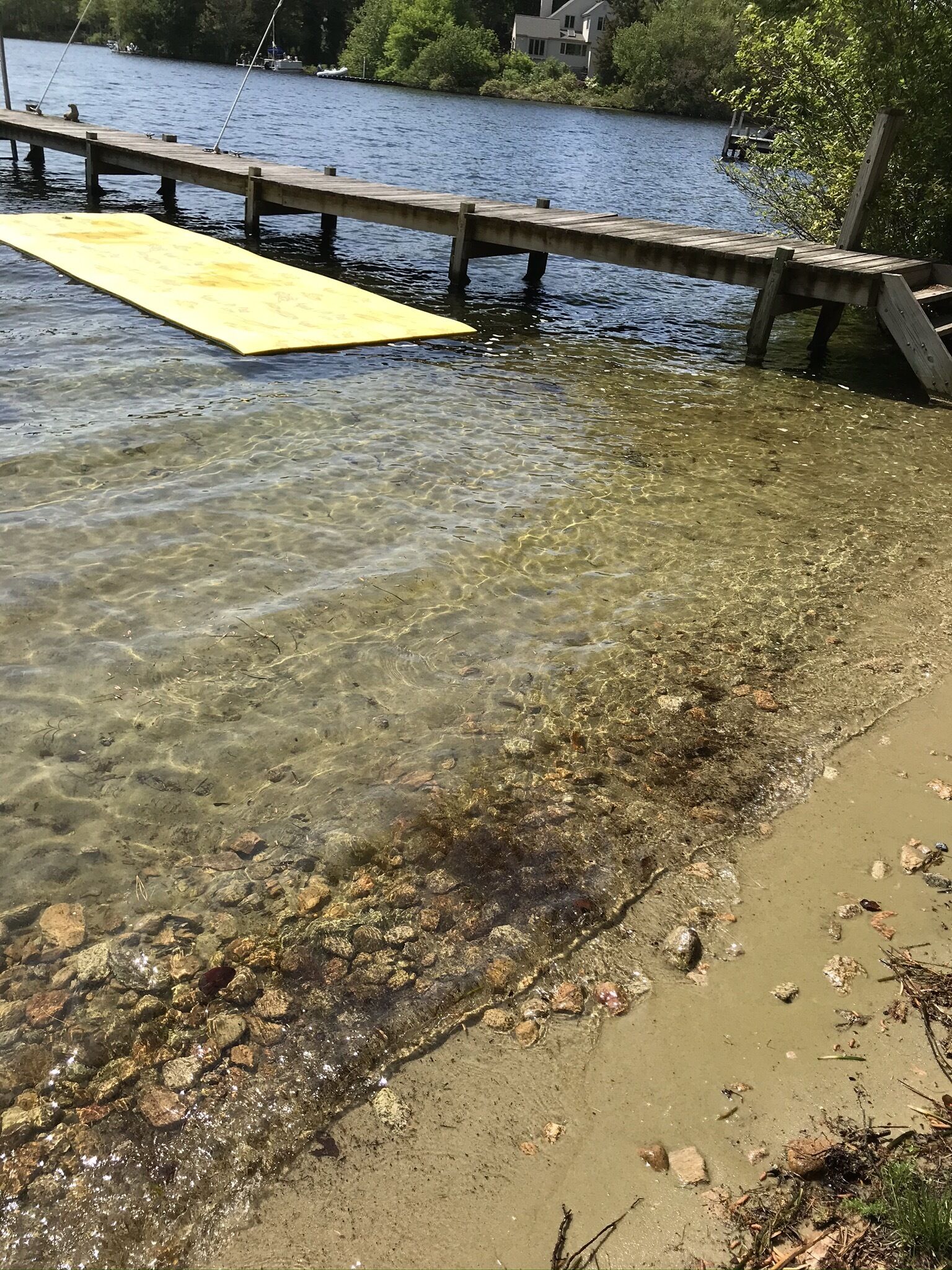 A wooden dock extending into a clear lake with visible rocks and a yellow floating platform.