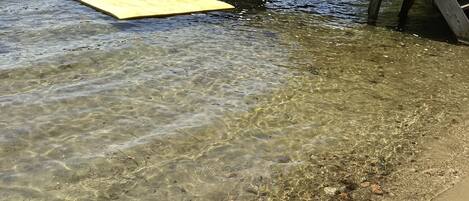 A wooden dock extending into a clear lake with visible rocks and a yellow floating platform.