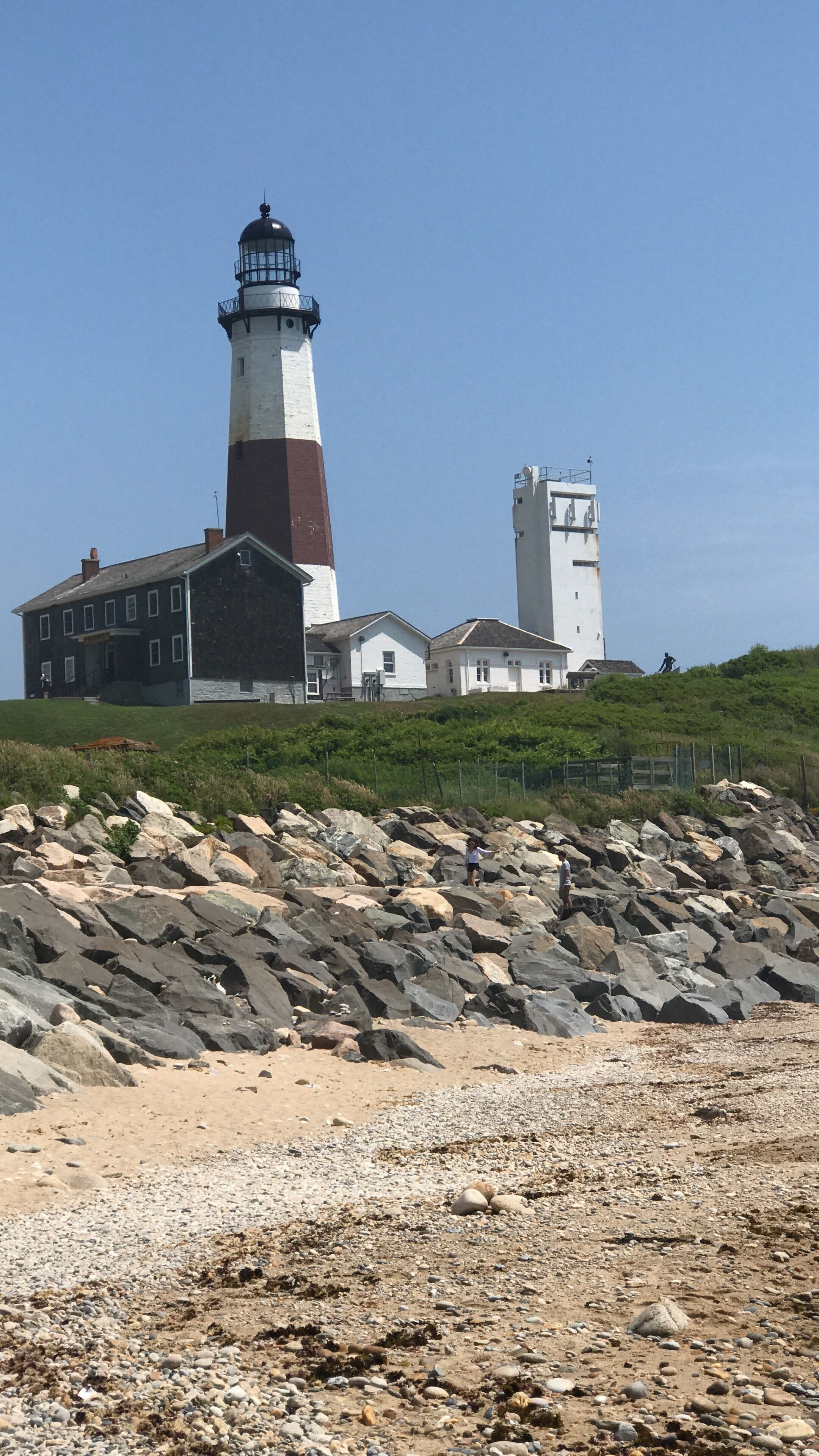 A lighthouse with a white and red tower, a large building with multiple windows, and a rocky shoreline.