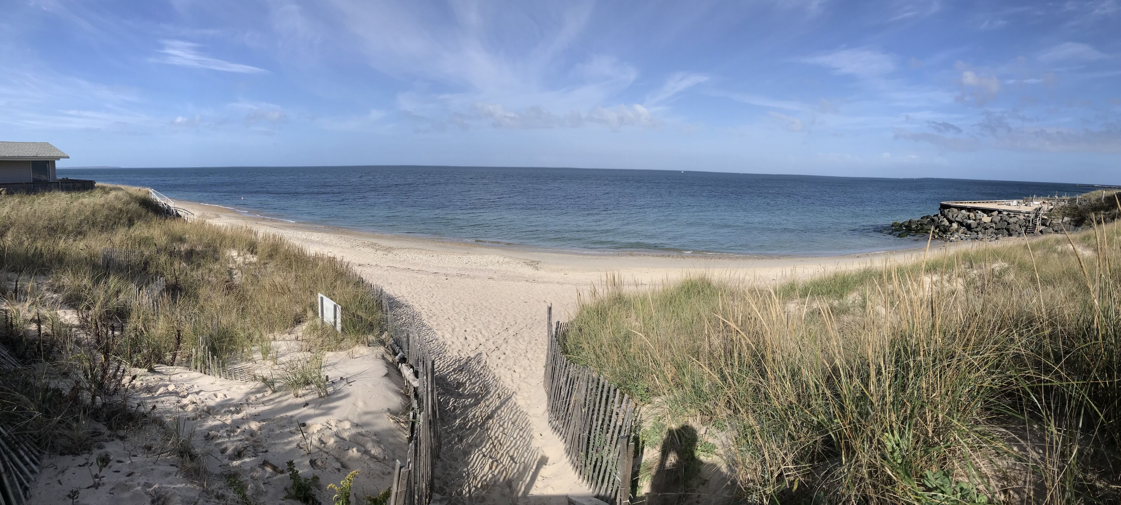 Een strand met een zandpad dat naar het water leidt, omringd door gras en een klein gebouw.