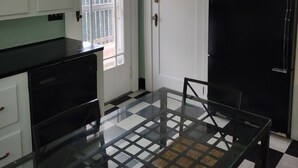 Een keuken met witte kasten, een zwarte koelkast, een glazen tafel en een geruite vloer.