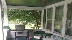 Een overdekte veranda met een witte bank, een klein tafeltje en een barbecue.