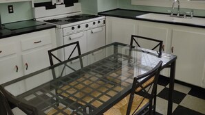 Een keuken met een glazen tafel, vier stoelen, een fornuis en een raam met zonwering.