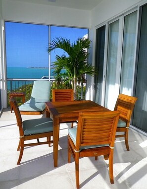 A balcony with a wooden table and chairs, a potted plant, and a view of the ocean. - Stunning Panoramic View - Oceanfront Villa - Calming Charm (Long Bay)