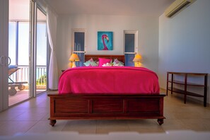 Un dormitorio con una cama grande, dos lámparas de noche, un cuadro en la pared y vistas a través de una puerta corrediza de vidrio.