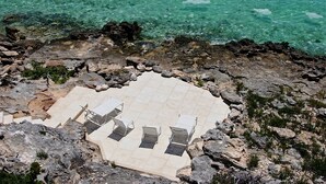 Una platja rocosa amb una zona enrajolada que inclou quatre gandules i una barana metàl·lica.
