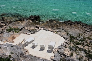 Una spiaggia rocciosa con una zona piastrellata, quattro lettini e un corrimano in metallo.