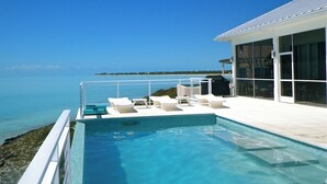 Zona de piscina moderna amb aigua blava cristal·lina, gandules blanques i vista a l'oceà.