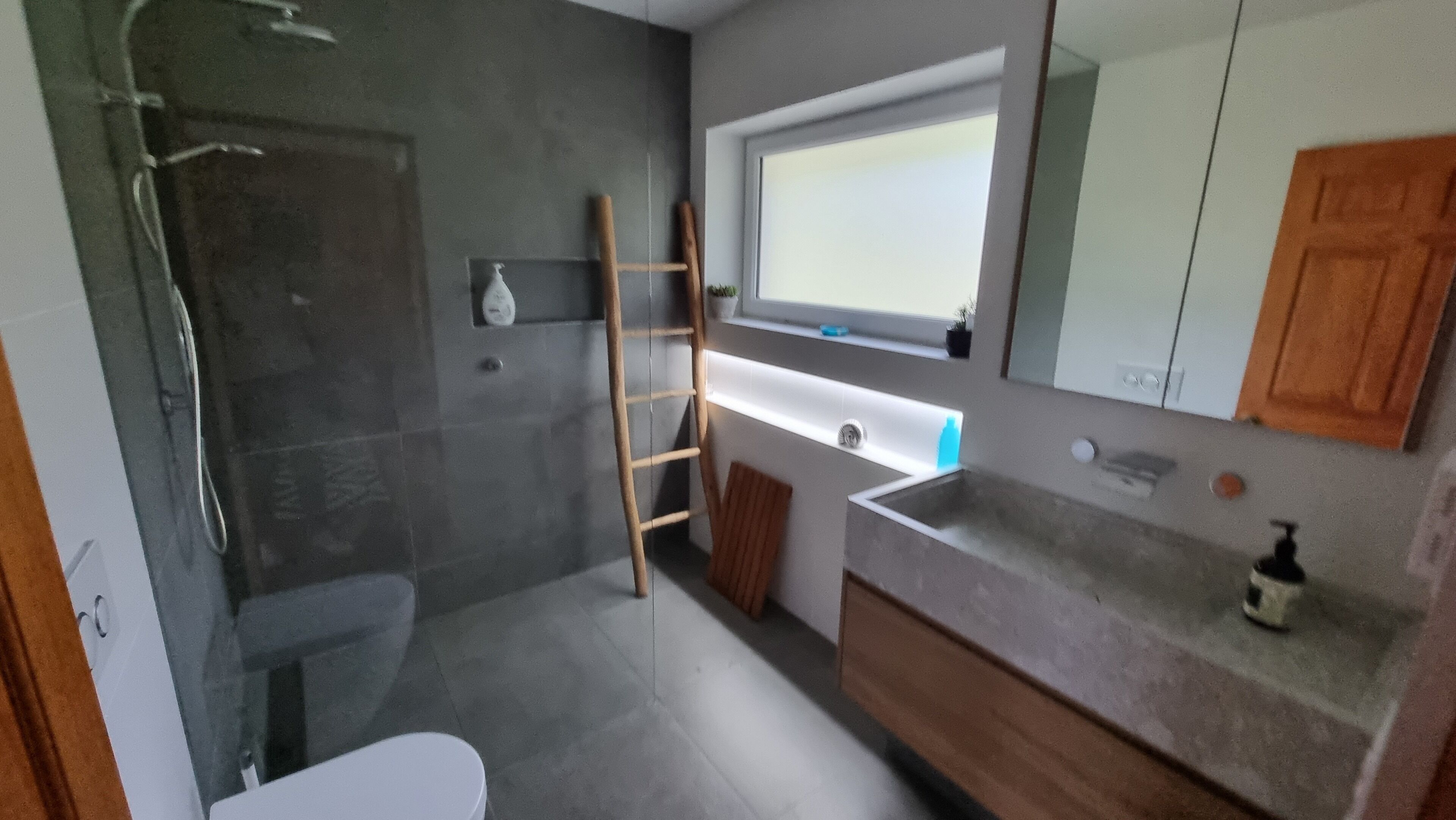 A bathroom with a shower, a toilet, a sink with a mirror, and a window above the sink.