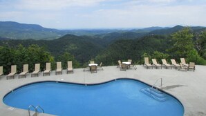 A swimming pool with lounge chairs and tables, surrounded by a concrete deck, overlooking a mountainous landscape. - Bears Abound-- a Dog-friendly, Log Cabin With Breathtaking Views (Sevierville)