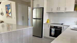 Una cocina moderna con gabinetes blancos, un refrigerador de acero inoxidable, horno empotrado y encimera de mármol.