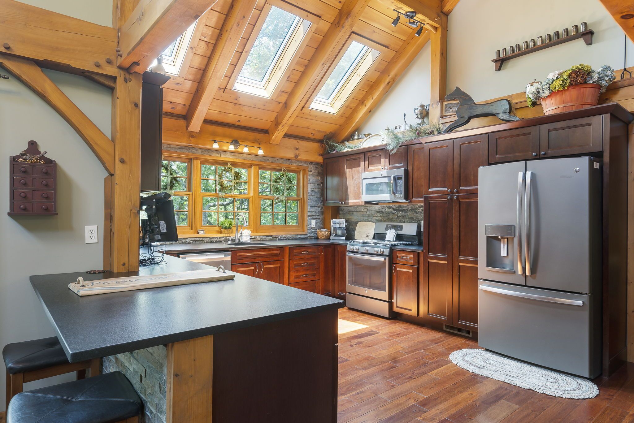 A kitchen with wooden beams, a large island, stainless steel appliances, and a view of the outdoors.