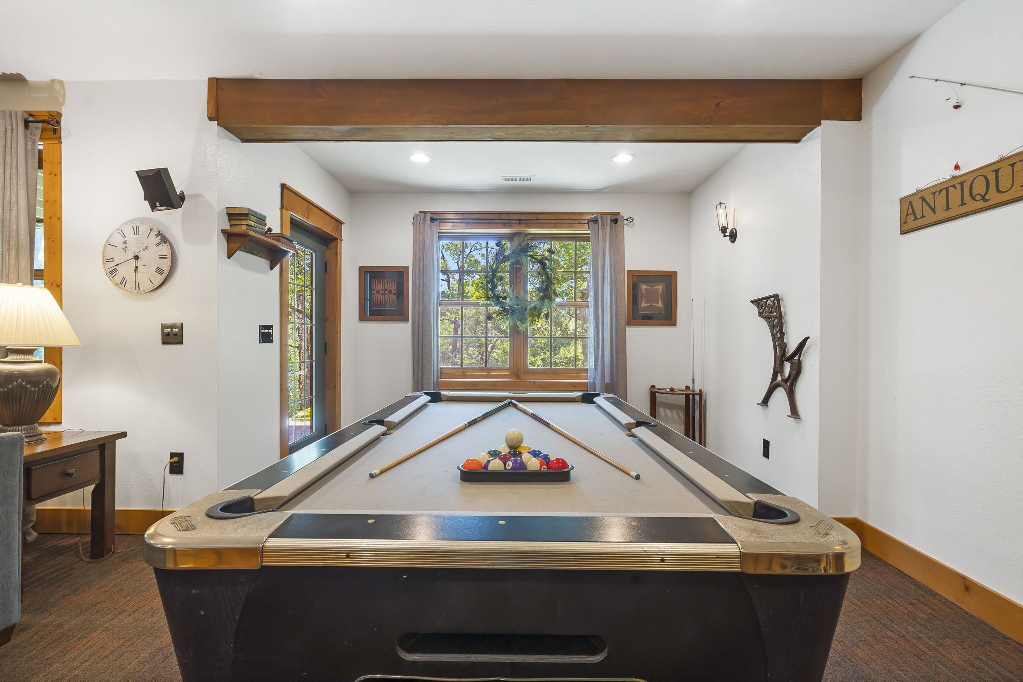 A pool table with balls, a clock, and a window with curtains.